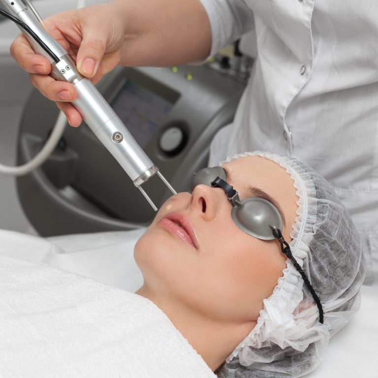 Woman lying on a table with protect glasses on eyes getting a laser skin treatment in healthy beauty spa salon